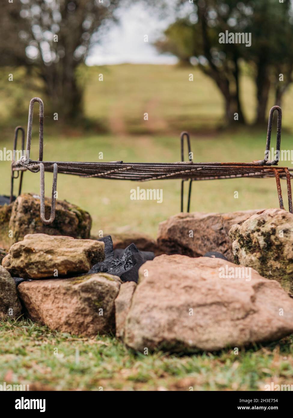 Grille métallique rouillée placée sur des pierres au-dessus du charbon sur un terrain herbacé au camping en journée Banque D'Images