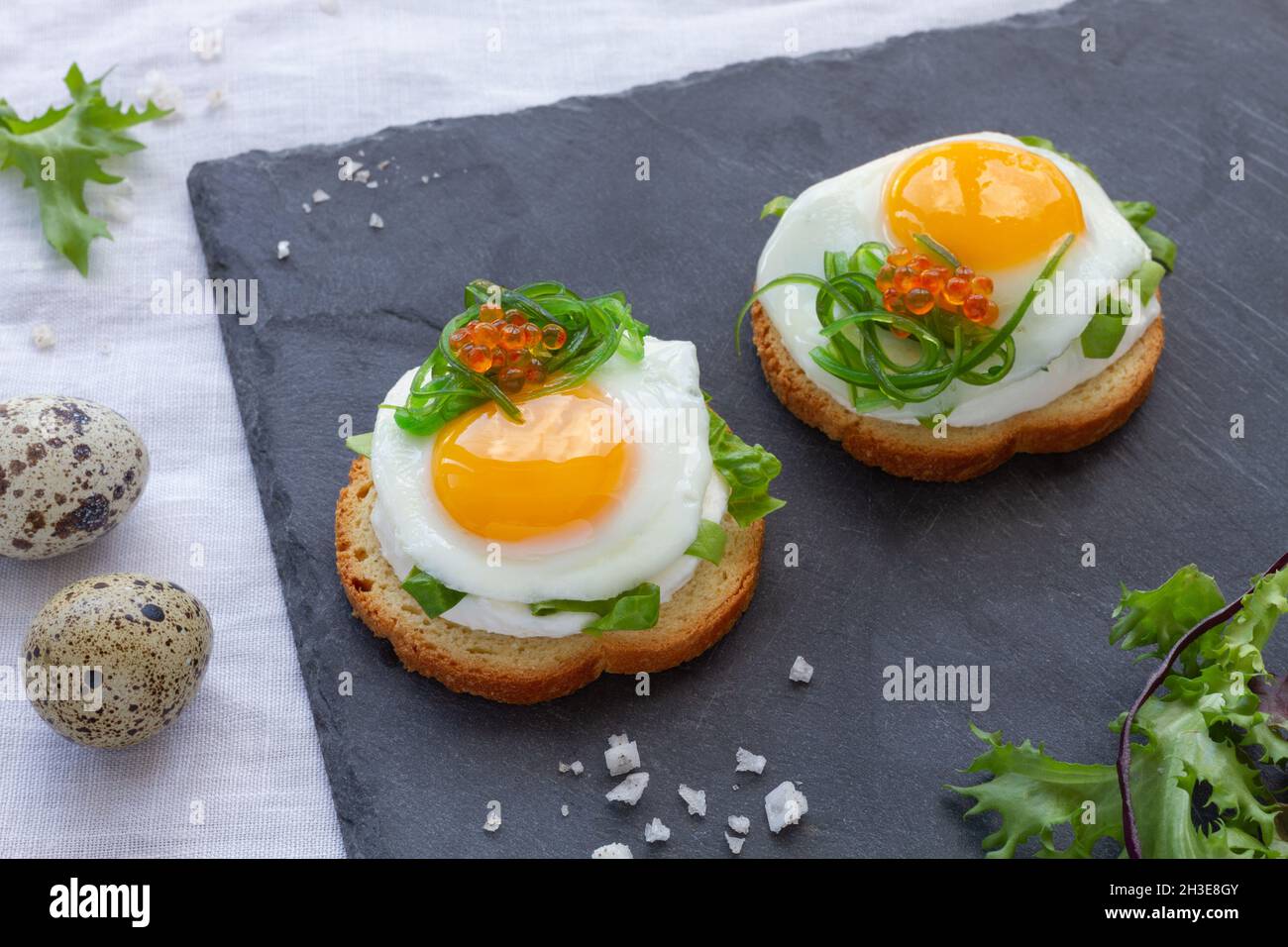 Des canapés appétissants avec du pain croustillant et des œufs de caille frits décorés d'herbes et de caviar servis sur un plateau gris Banque D'Images
