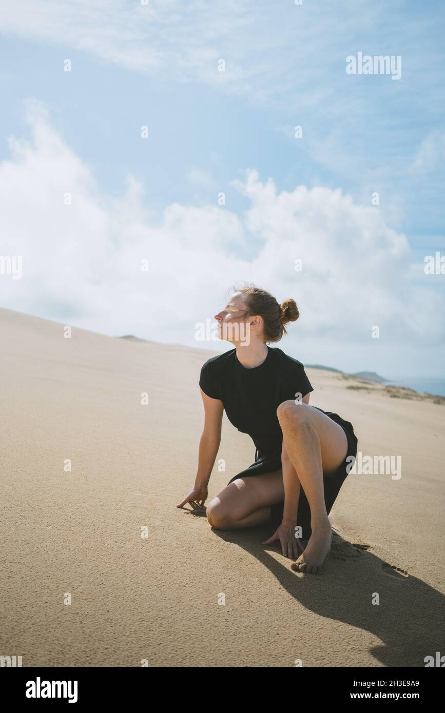 Vue latérale du corps d'une femme pieds nus se penchant sur les mains tout en se squatant sur une dune de sable dans un désert chaud Banque D'Images