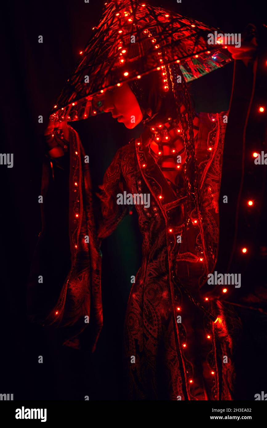 Femme énigmatique dans une tenue traditionnelle créative et coiffeuse vietnamienne avec éclairage rouge dans un studio sombre sur fond noir pendant la perfo Banque D'Images