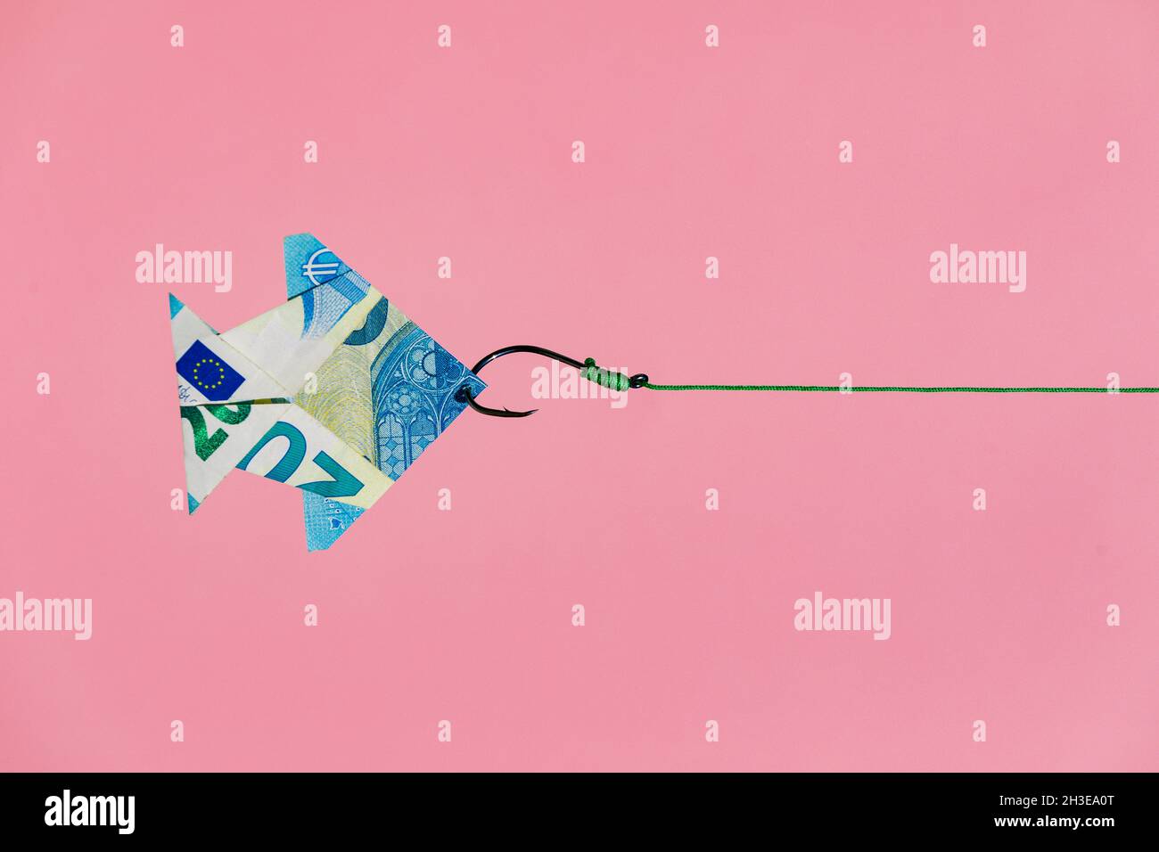 Crochet sur la ligne tirant des poissons d'origami en forme de billet de banque en euros comme concept de richesse et de l'argent gagnant sur fond rose Banque D'Images