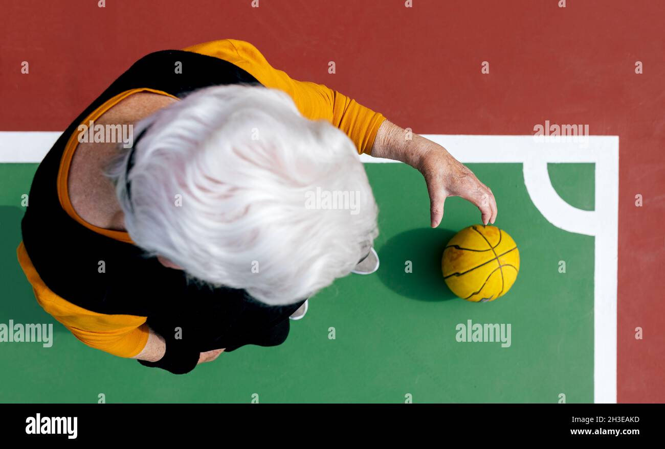 Vue de dessus d'une femelle mature anonyme avec des cheveux gris debout sur le terrain de sport avec du ballon tout en jouant au basket-ball Banque D'Images