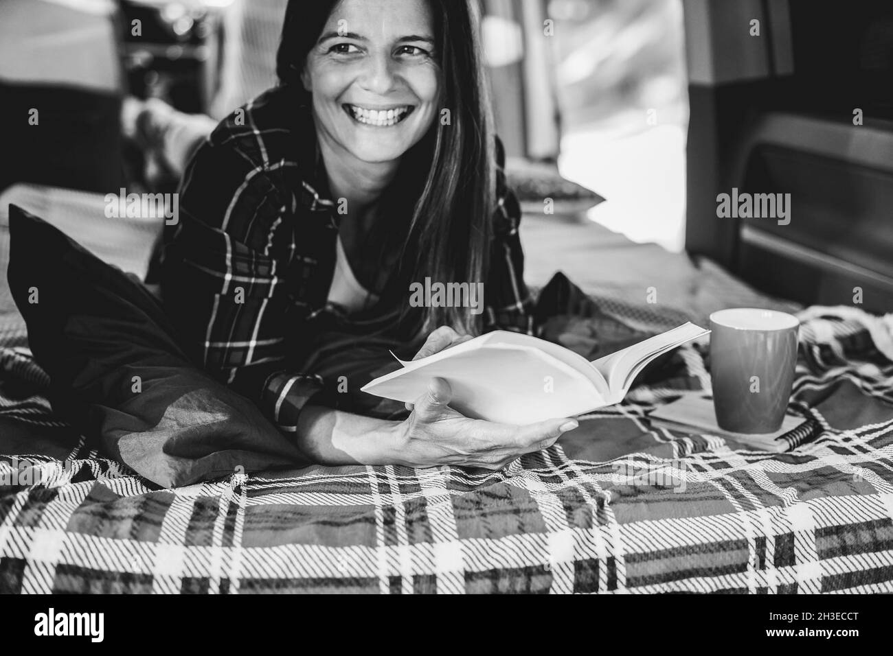 Femme âgée s'amusant à l'intérieur d'une camionnette de camping-car en lisant un livre et en buvant du café - Focus sur la main gauche Banque D'Images