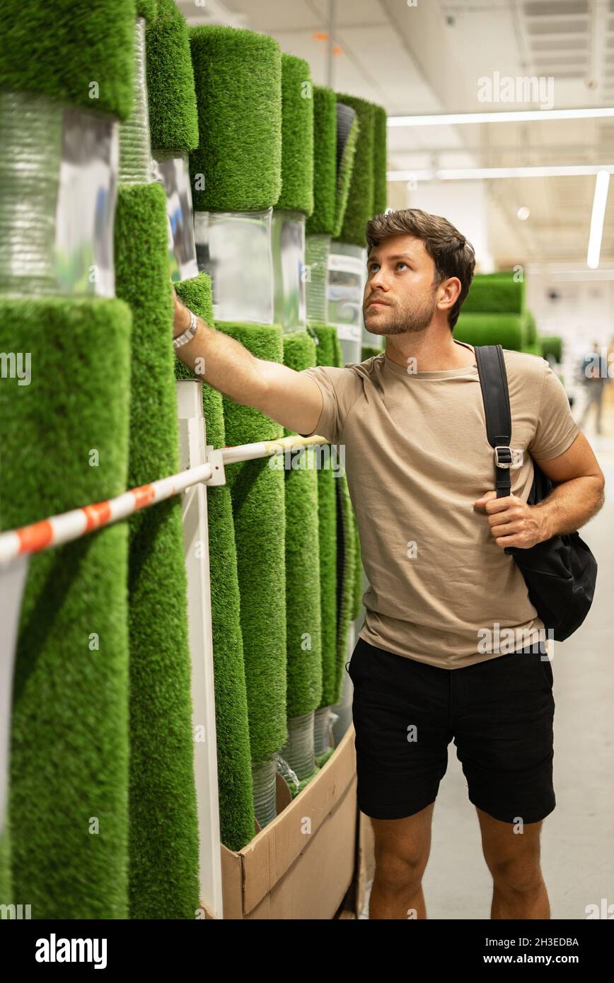 Décontracté homme magasiner dans le département de plancher et les biens de maison tout en choisissant l'herbe artificielle roulée Banque D'Images