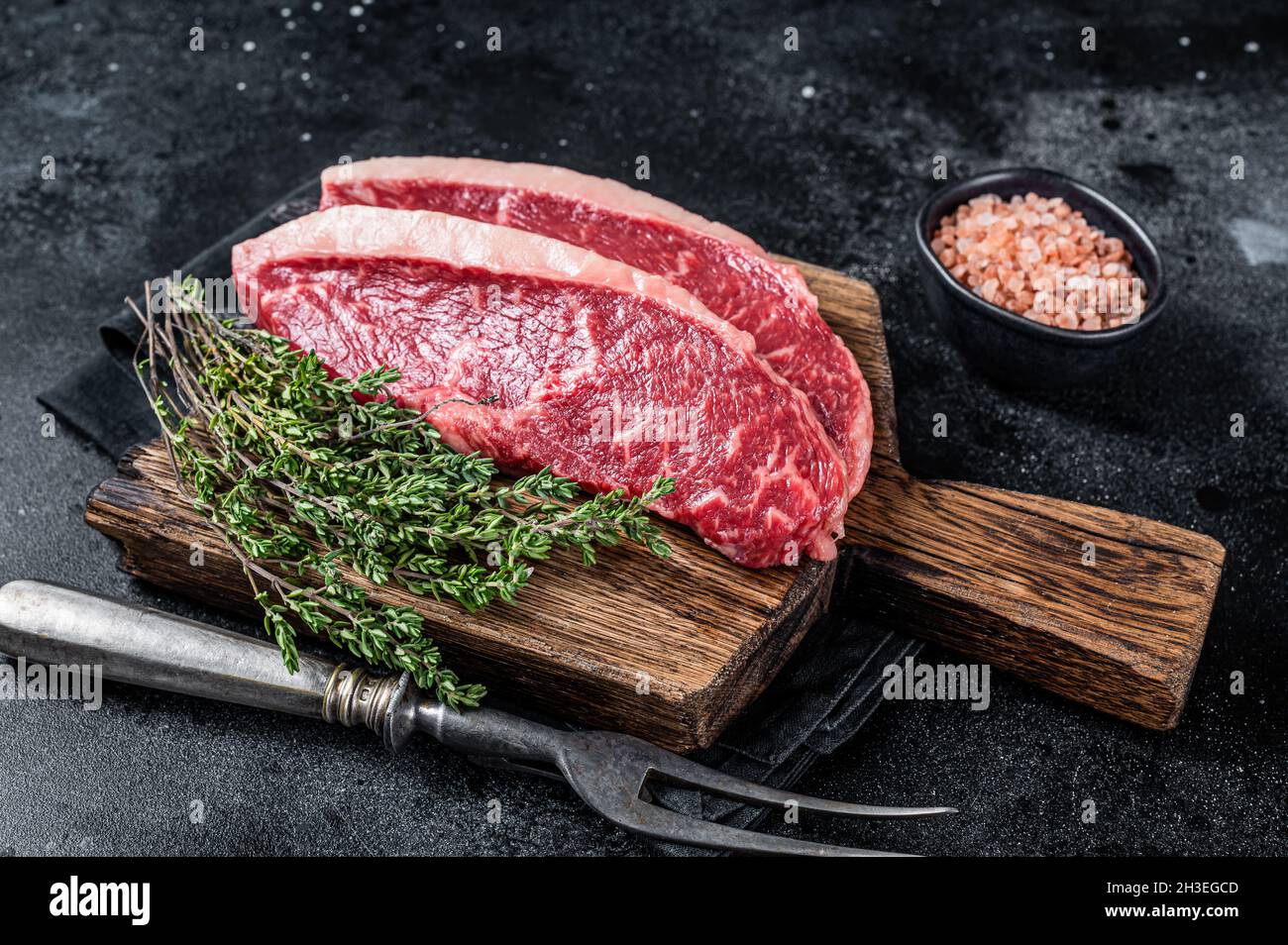 Steak de rumsteck cru non cuit ou biftecks de viande de bœuf au chapeau de sirloin sur une planche de bois. Arrière-plan noir. Vue de dessus Banque D'Images
