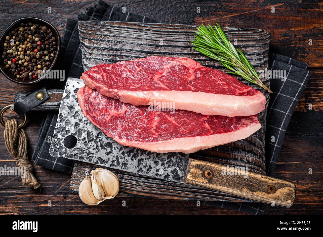 Steaks de viande de bœuf sur le dessus de la cicloine crue sur le butboard avec le cale à viande. Arrière-plan sombre. Vue de dessus Banque D'Images