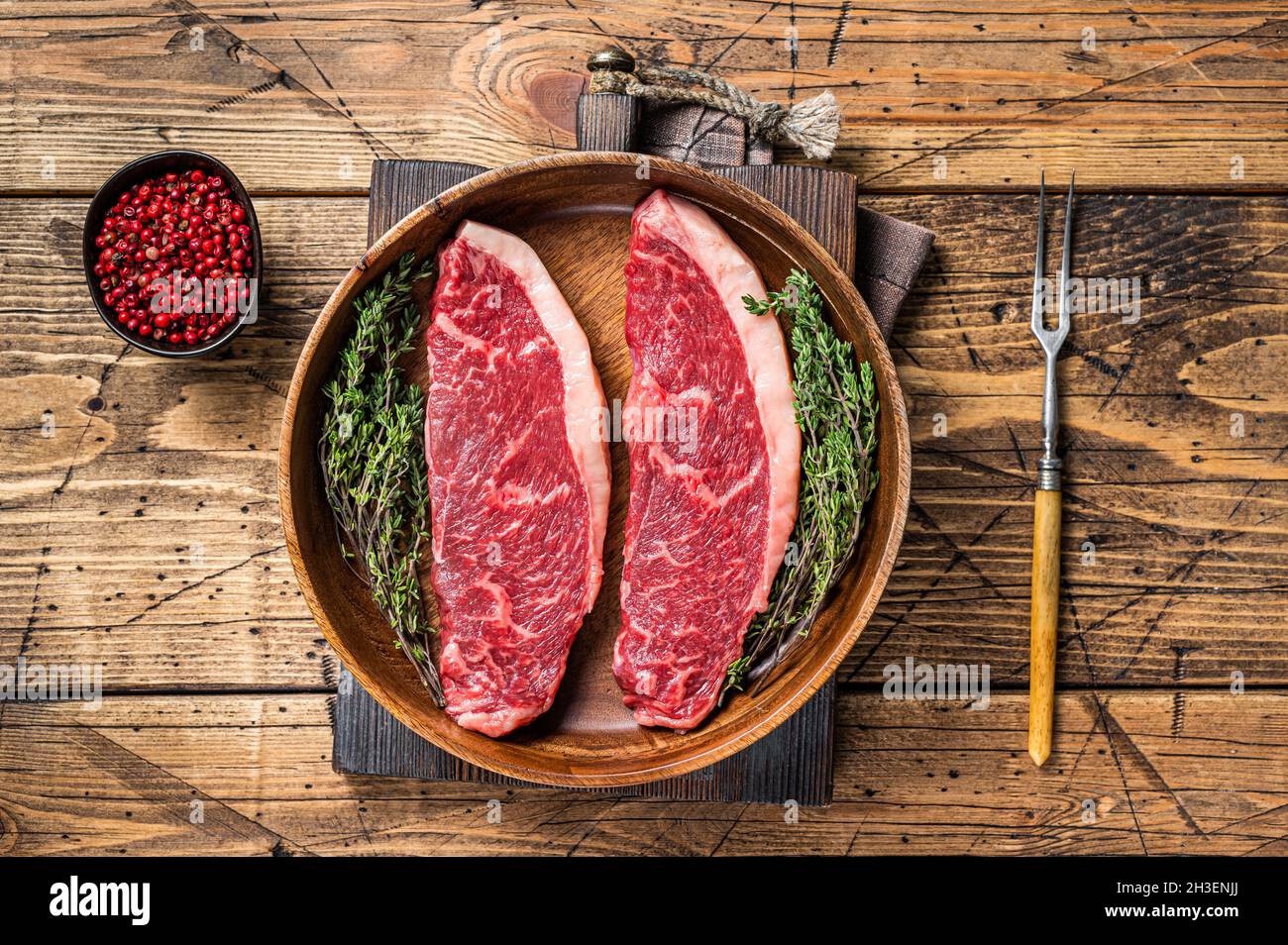 Steaks de viande de boeuf non cuits en haut cru au sommet de sirloin dans une assiette en bois avec des herbes. fond de woden. Vue de dessus Banque D'Images