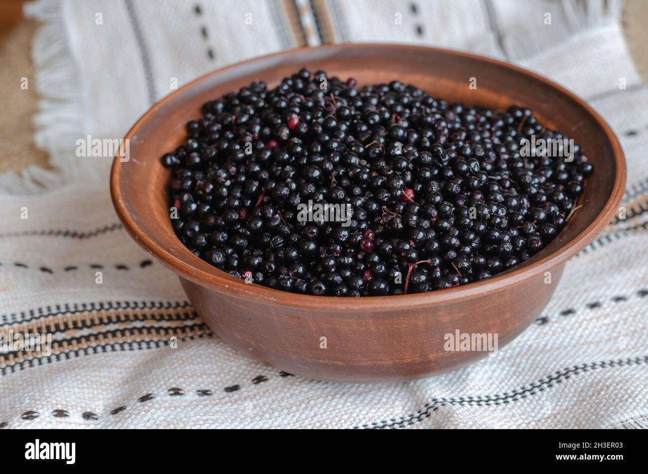 Baies de sureau noires mûres dans un bol brun.Bol en argile sur une nappe ethnique en lin.Sambucus nigra.Mise au point sélective. Banque D'Images