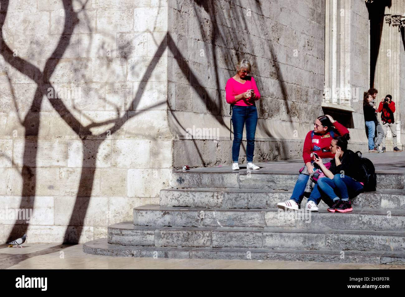 Les touristes s'assoient sur les marches de la Calle de la Lonja Valencia Old Town Espagne ombres d'arbres sur le mur Banque D'Images