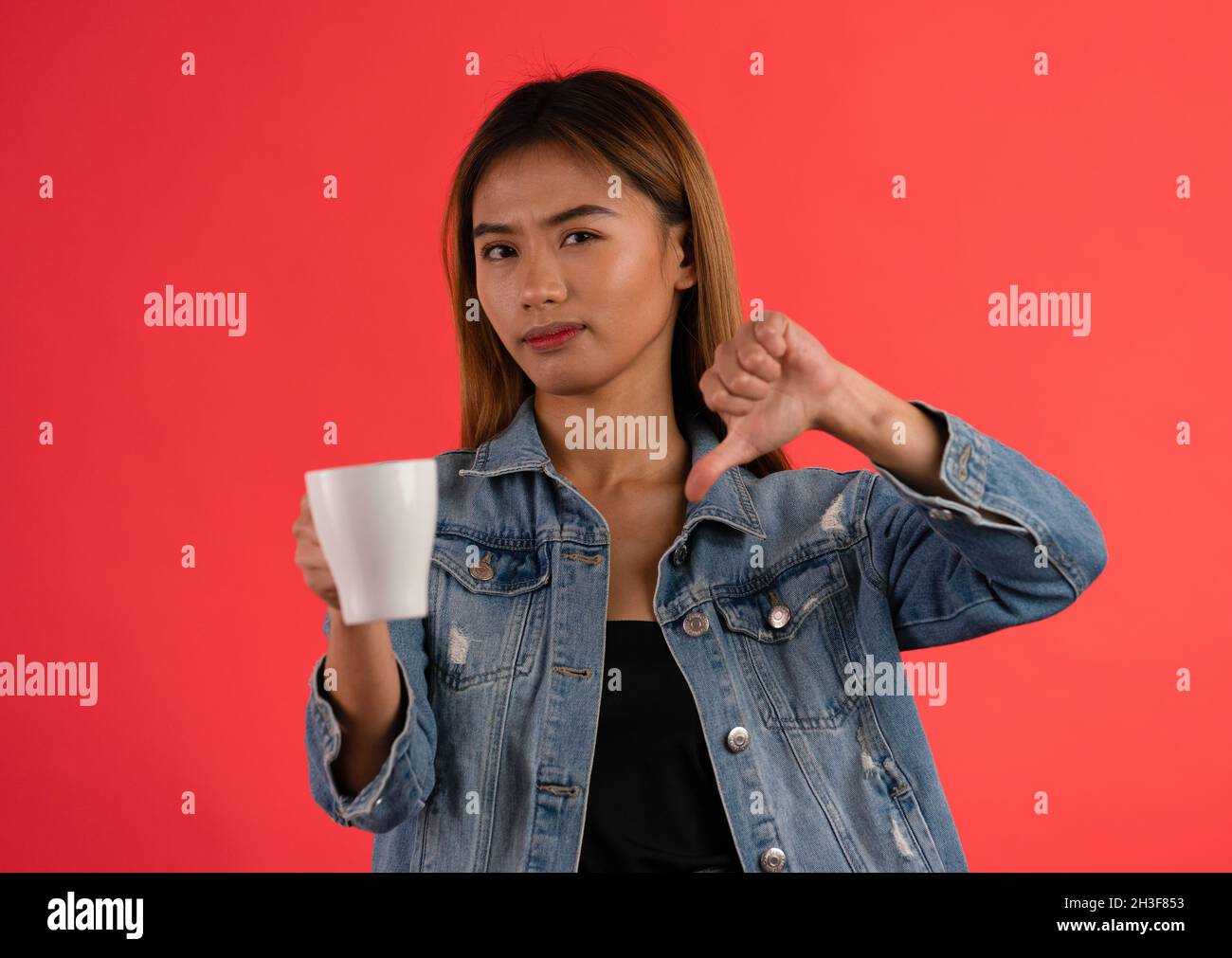 Jeune femme asiatique attrayante déçue tenant un café avec les pouces en studio Banque D'Images