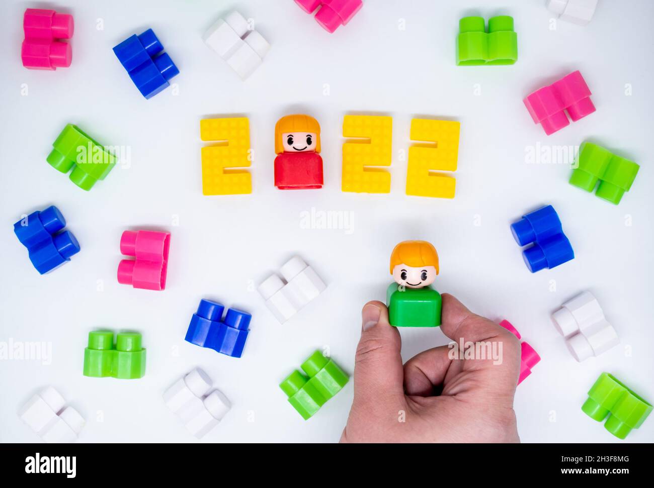 Blocs de construction colorés, jouets figures en plastique: Fille en 2022 chiffres, garçon en main, fond blanc. Banque D'Images