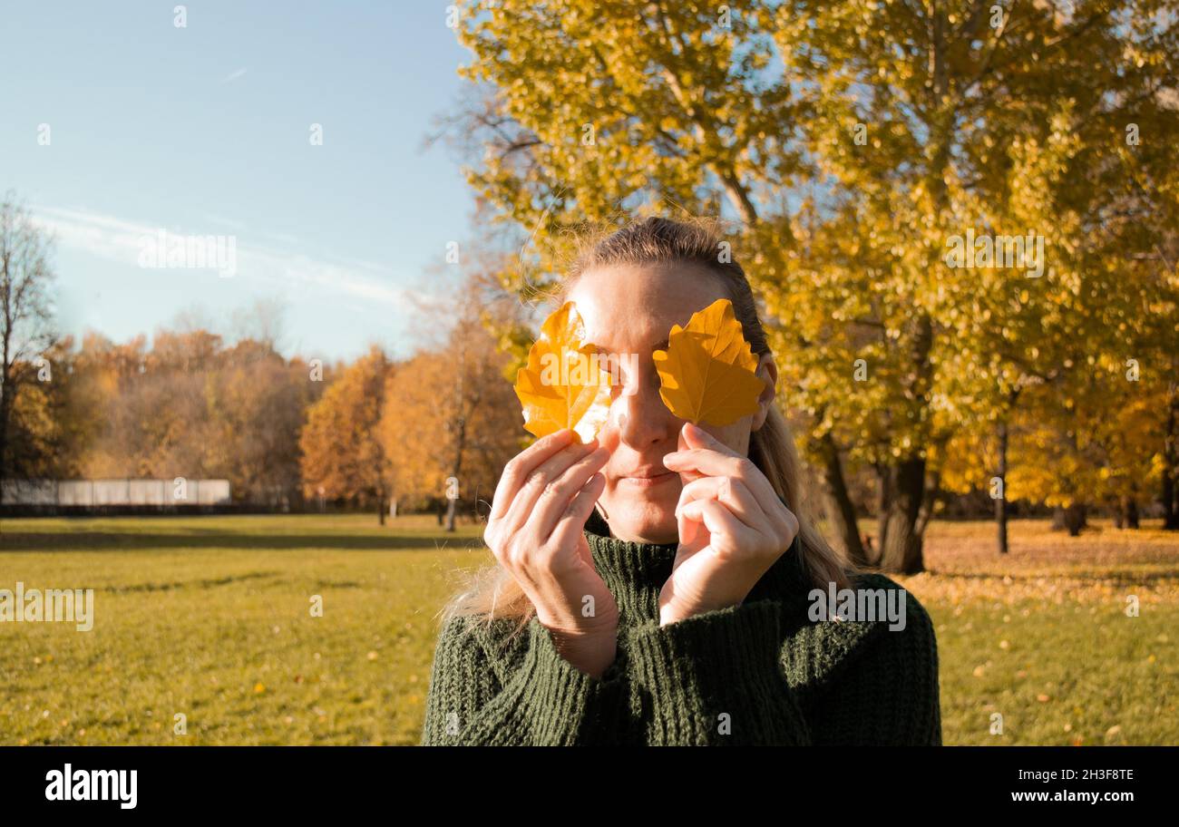 Portrait de femme avec les yeux fermés tient deux feuilles jaunes, les mains gros-sur, arrière-plan arbres d'automne. Banque D'Images