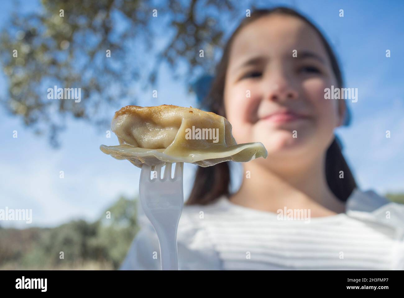 Enfant fille avec un morceau de jiaozi sur la fourchette.Arrière-plan extérieur Banque D'Images