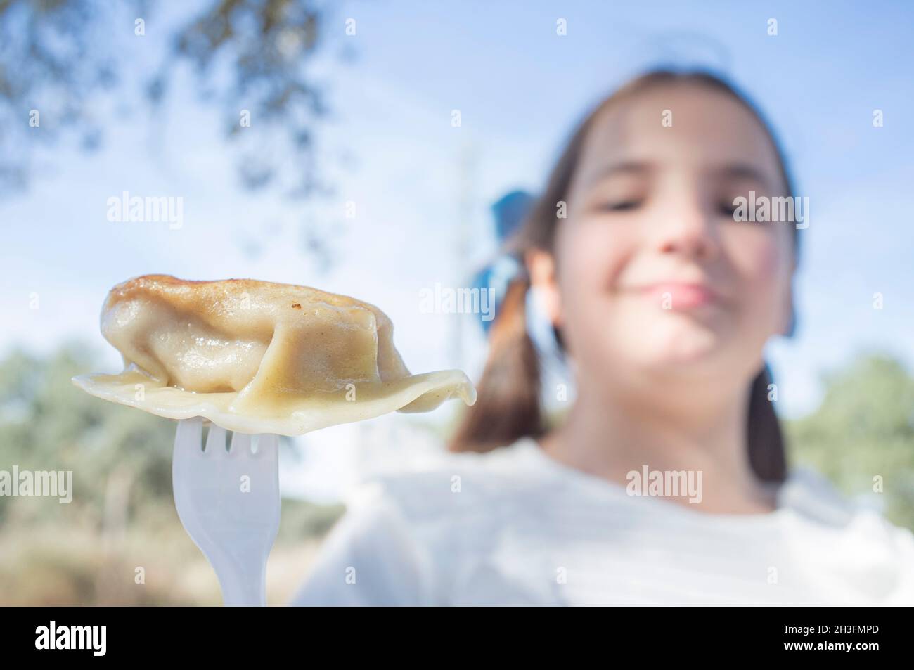 Enfant fille avec un morceau de jiaozi sur la fourchette.Arrière-plan extérieur Banque D'Images