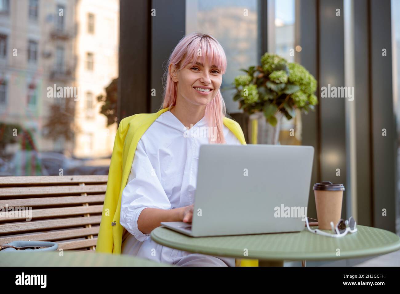 Une jeune femme joyeuse utilisant un ordinateur portable dans un café en plein air Banque D'Images