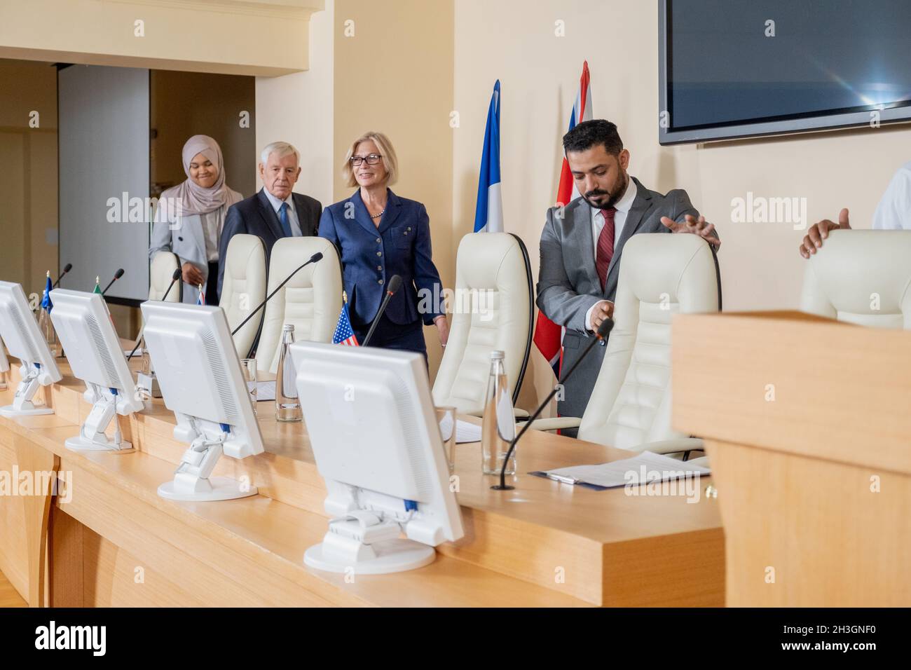 Groupe de participants multiethniques entrant dans la salle de conférence et prenant des sièges devant les moniteurs Banque D'Images