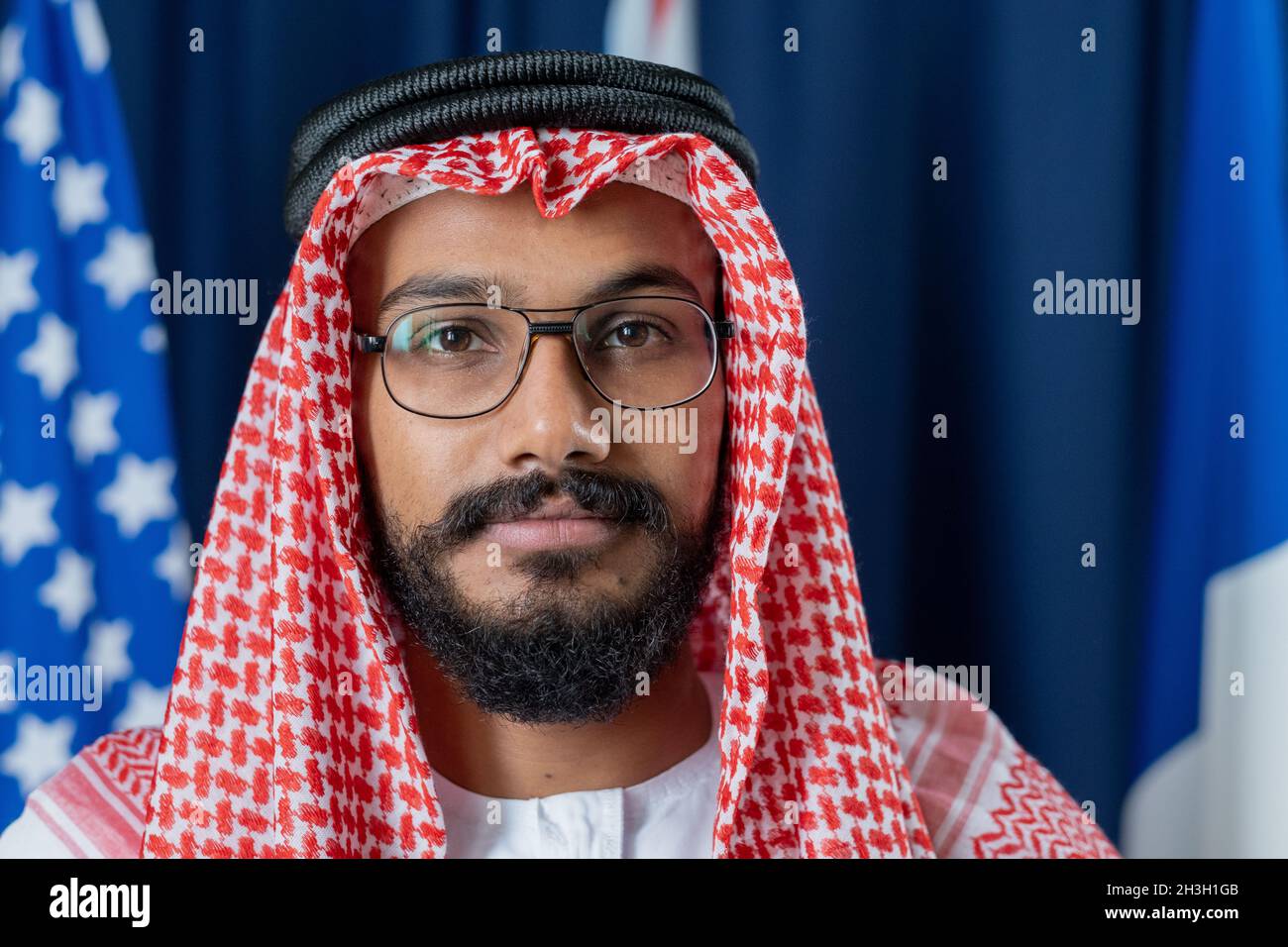 Portrait d'un homme politique musulman sérieux et confiant, vêque de robe nationale, posé contre des rideaux et des drapeaux bleu foncé Banque D'Images