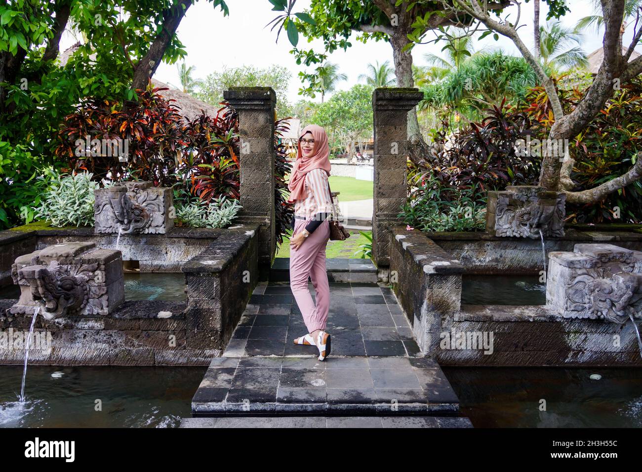 Portrait de la jeune femme musulmane asiatique portant le hijab pose dans le jardin avec étang et fontaine d'eau à Bali.Sourire et expression heureuse. Banque D'Images