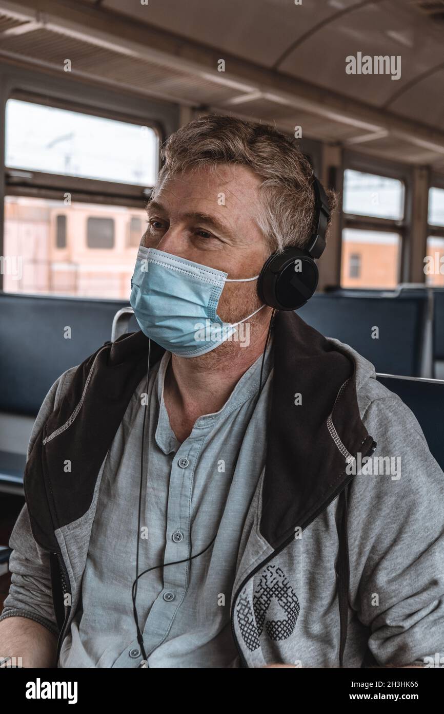 Portrait d'un homme adulte sérieux portant un casque avec un masque de protection médicale sur son visage dans les transports publics près de la fenêtre.Mesure préventive. Banque D'Images