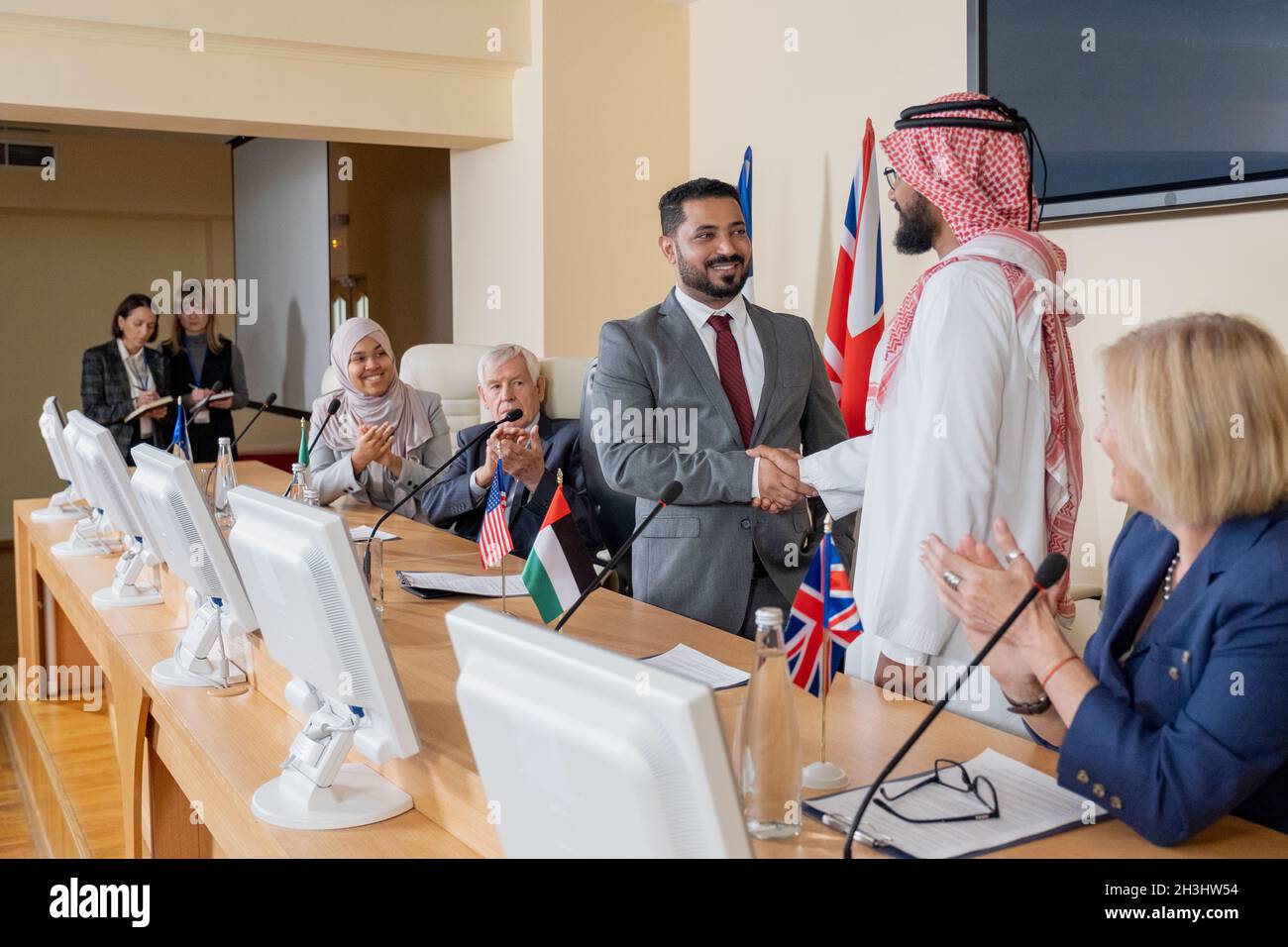 Un homme politique souriant de race mixte en costume fait la poignée de main avec des représentants arabes en thobe à la conférence Banque D'Images