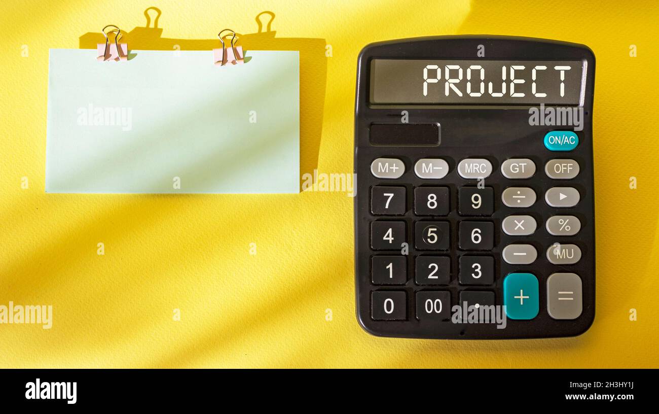 Sur fond jaune se trouve une calculatrice avec le texte Project, à côté d'un autocollant pour écrire Banque D'Images