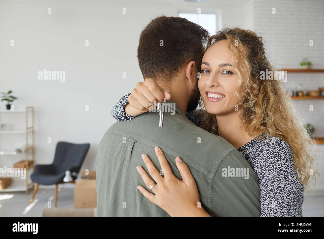 Bonne jeune femme embrassant son mari, tenant la clé de leur nouvelle maison et souriant Banque D'Images