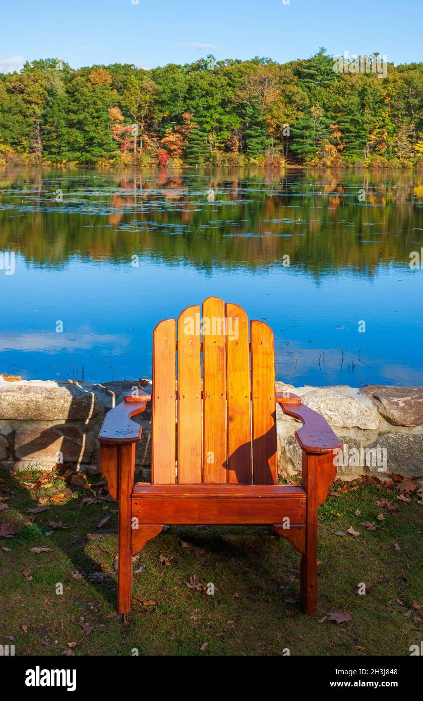 Chaise Adirondack en face d'un lac, par un mur de pierre de soutènement. Forêt mixte avec des arbres aux couleurs d'automne en arrière-plan. Moore State Park, Paxton, Massachusetts Banque D'Images