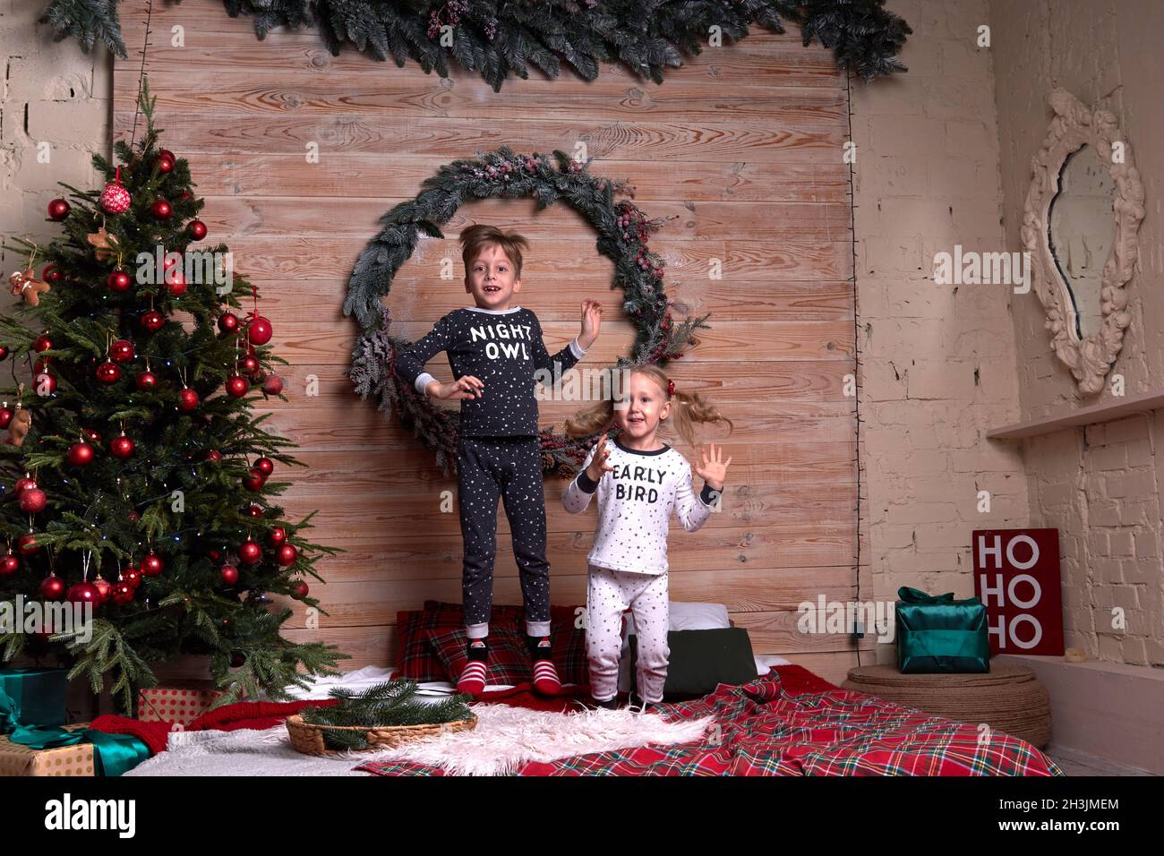 Les enfants de la même famille regardent un pyjama doux et chaud jouant à la maison le soir de noël sous un arbre de Noël décoré.Un enfant heureux qui saute sur le lit. Banque D'Images