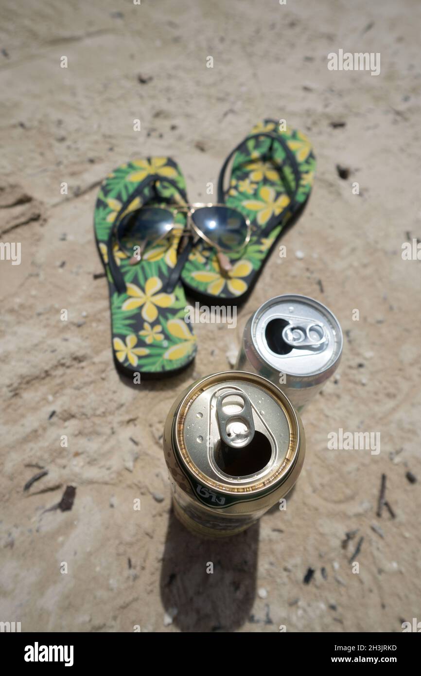 Flipflops, lunettes de soleil et boîtes de boissons sur une plage de sable Banque D'Images