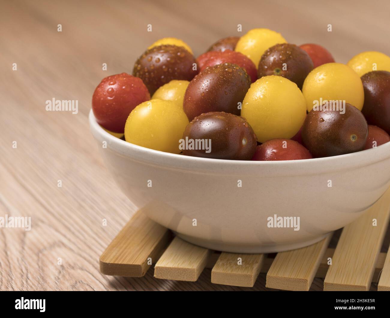 Les tomates cerise dans une variété de couleurs dans un bol en céramique sur fond de bois. Banque D'Images