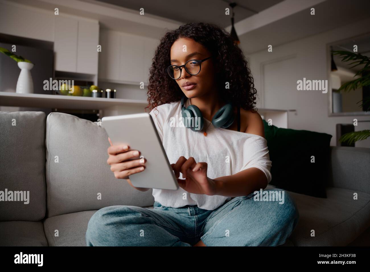 Femme multi-ethnique avec des lunettes utilisant une tablette tout en étant assis sur le canapé, contenu Banque D'Images