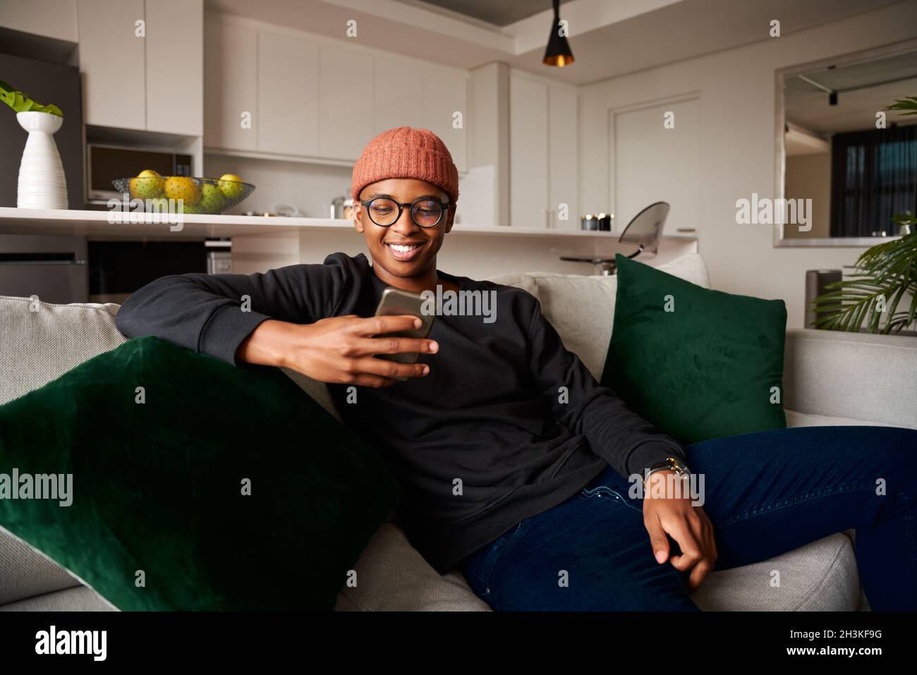 Homme noir adulte souriant en regardant le téléphone portable.Appartement moderne sur le canapé Banque D'Images