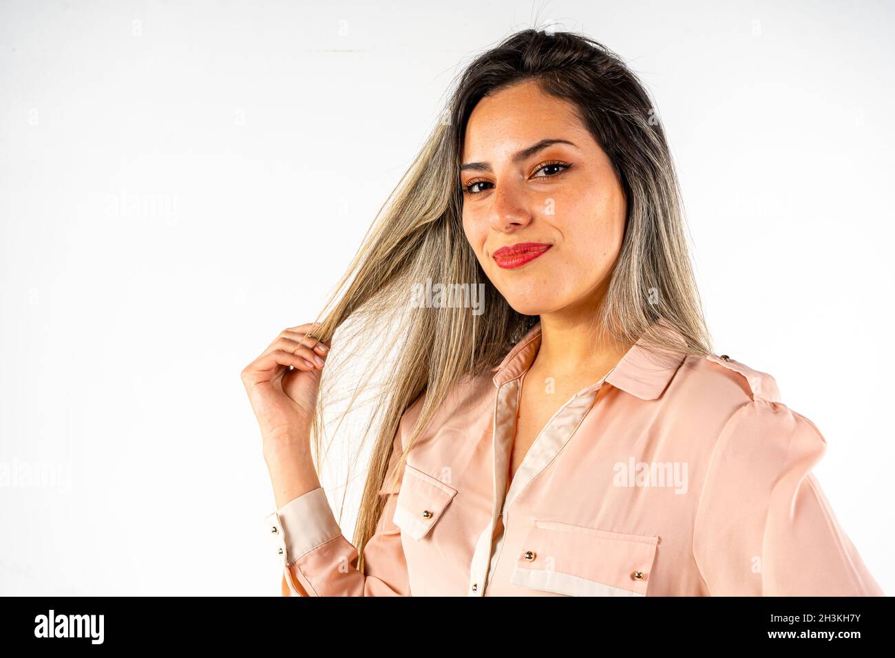 Portrait d'une belle femme latine souriante prenant une serrure de ses cheveux et avec un regard sensuel sur fond blanc, copier l'espace sur la droite pour la promotion Banque D'Images