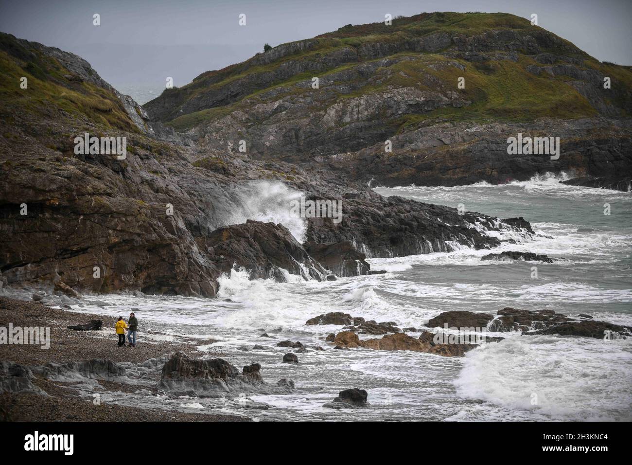 Swansea, pays de Galles.28 octobre 2021, Royaume-Uni Météo deux personnes profiter d'une promenade sur la plage à Bracelet Bay à Mumbles, comme les vagues se brisent contre les rochers lors d'une journée humide et venteuse dans le sud du pays de Galles. Banque D'Images