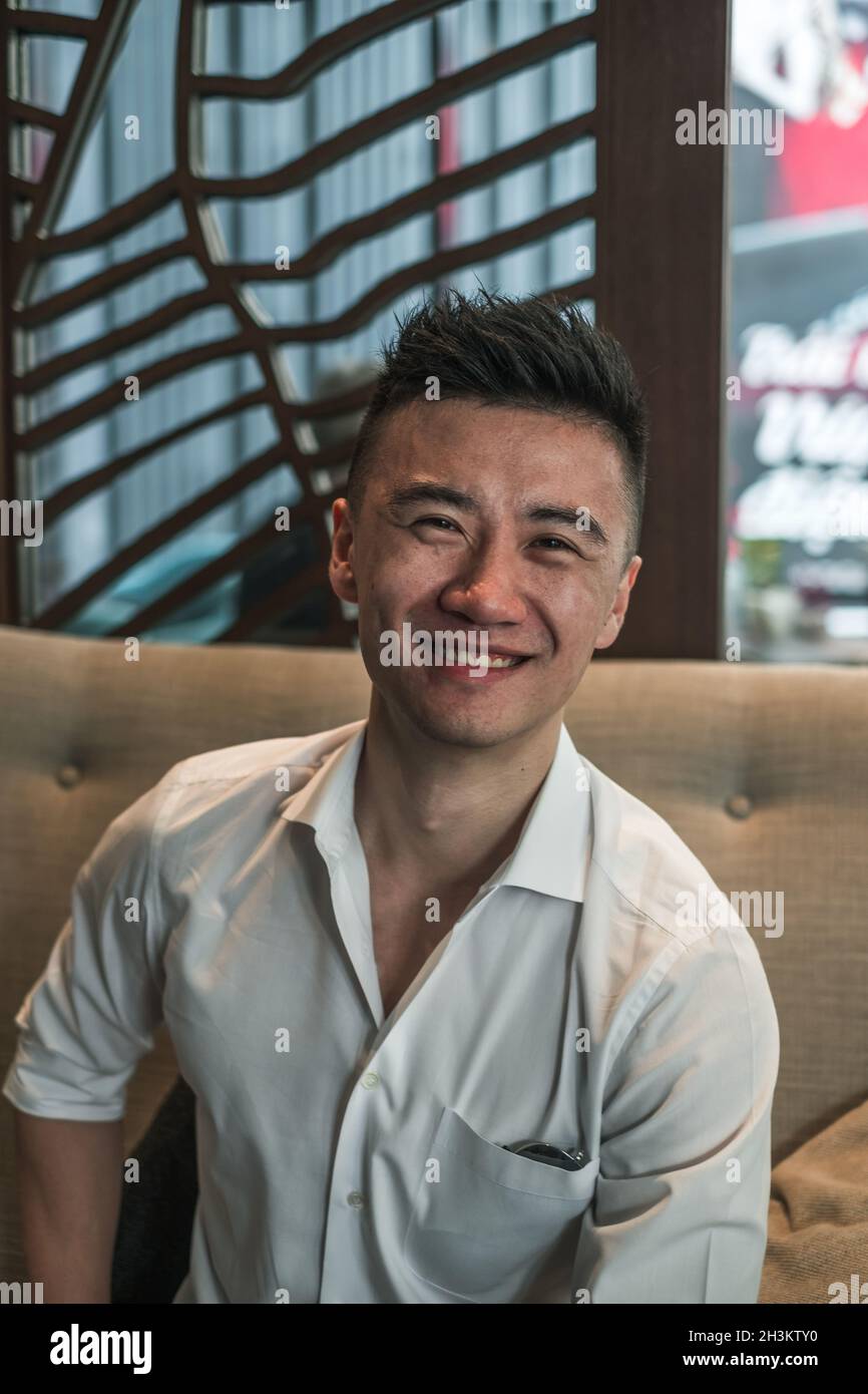 Portrait d'un jeune asiatique beau homme en chemise noire, assis dans un café et souriant.Un sourire charmant, une personne heureuse, la vie de la génération du millénaire, le style de vie Banque D'Images