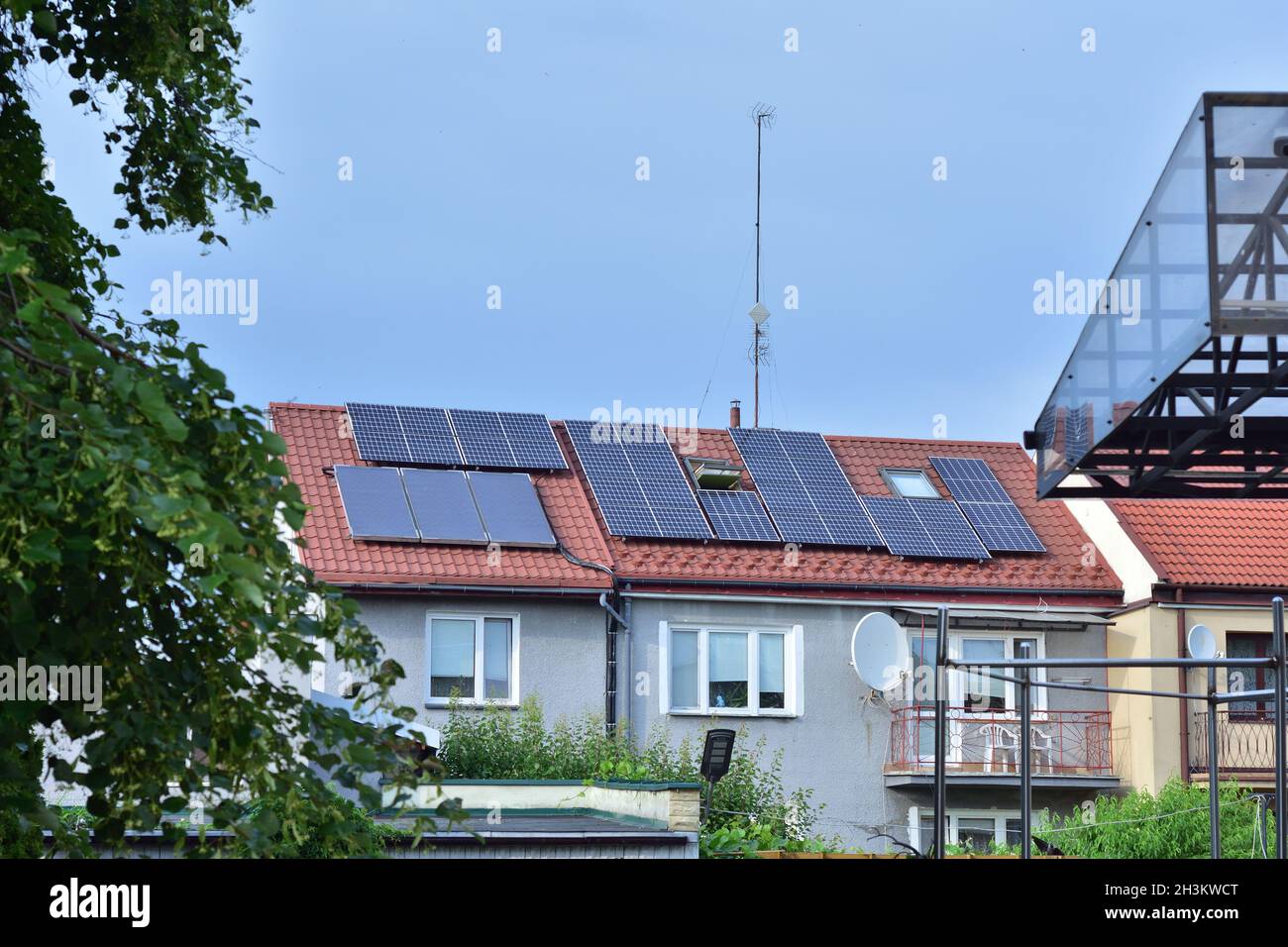 Panneaux solaires sur le toit d'une petite maison familiale, arbres et ciel. Banque D'Images