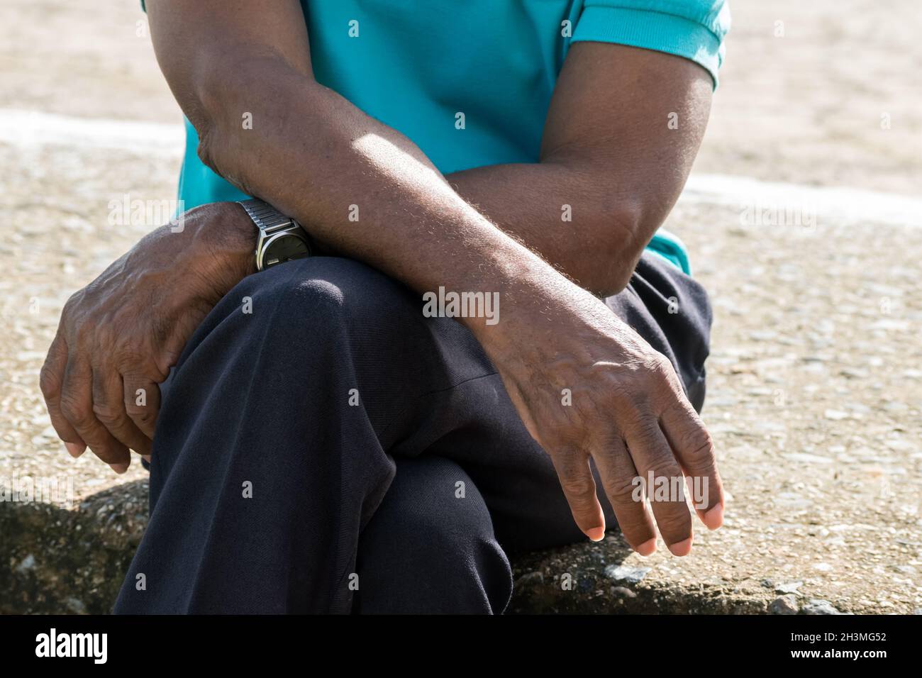 Gros plan sur les bras et les mains d'un homme âgé à peau foncée.Il est assis sur une surface semblable à une pierre et ses bras sont croisés sur ses genoux. Banque D'Images