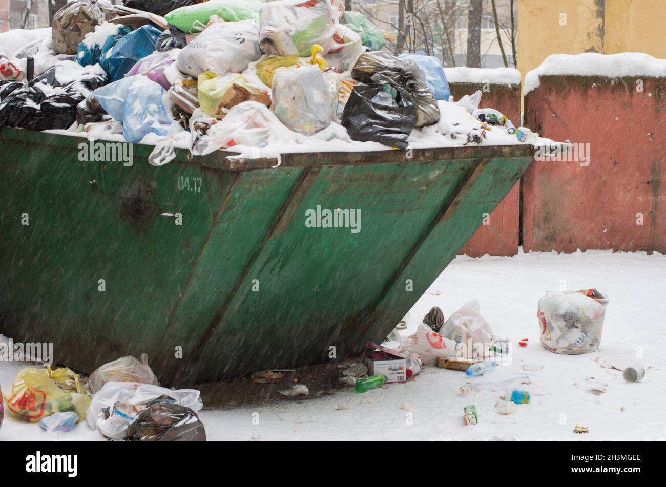 Saint-Pétersbourg, Russie - 26 janvier 2019 : benne à ordures débordant de sacs en plastique et de déchets ménagers et d'une zone polluée pendant une chute de neige Banque D'Images