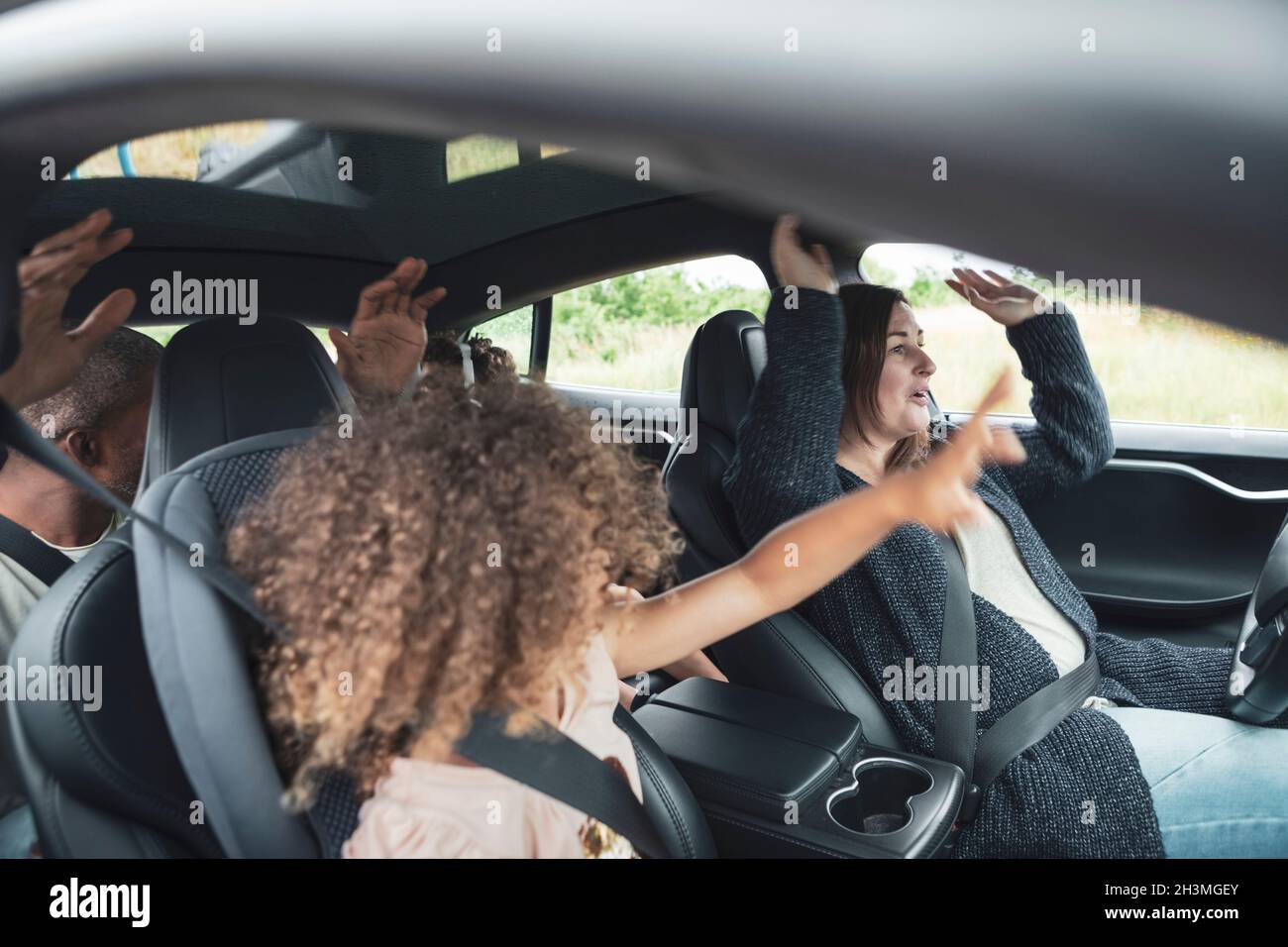 Famille heureuse avec les mains levées assis dans la voiture électrique Banque D'Images