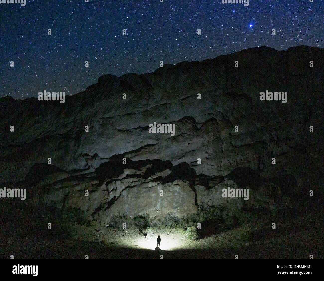 Homme en face d'une grande grotte avec une lampe de poche entourée d'étoiles Banque D'Images