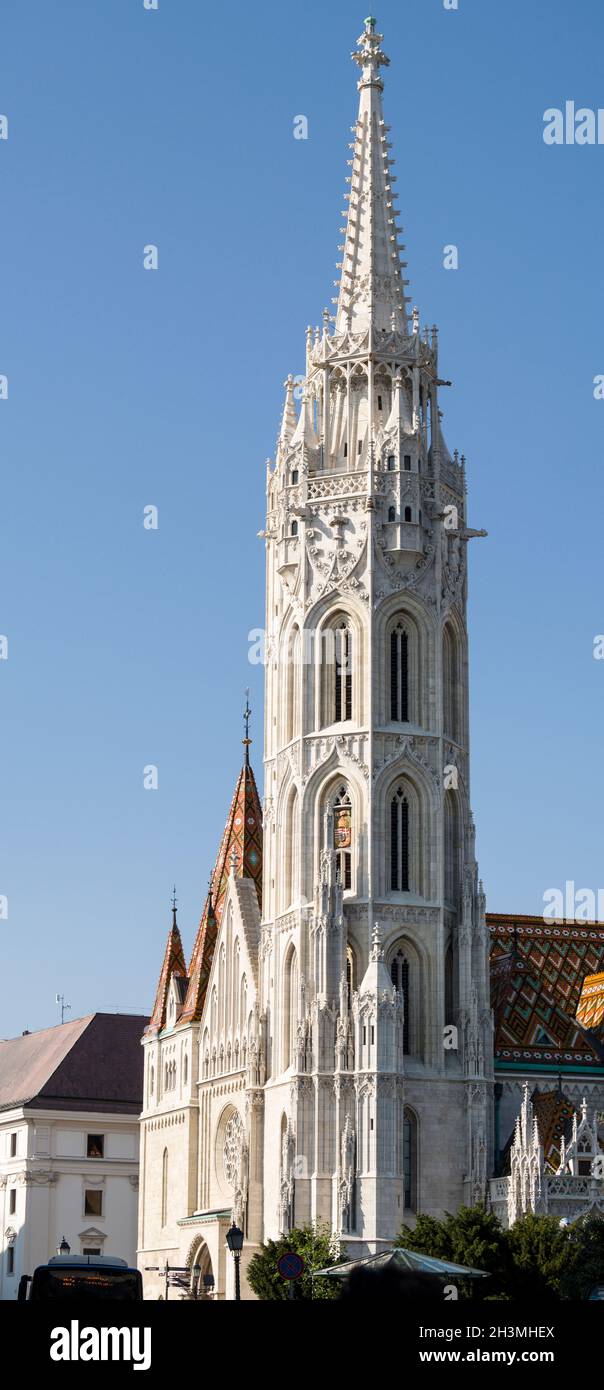 Le Spire de l'église Mathias à Buda: La tour en pierre blanche brille contre un ciel bleu les tuiles de toit décorées du bâtiment principal sont en dessous.L'église de l'Assomption du château de Buda Banque D'Images