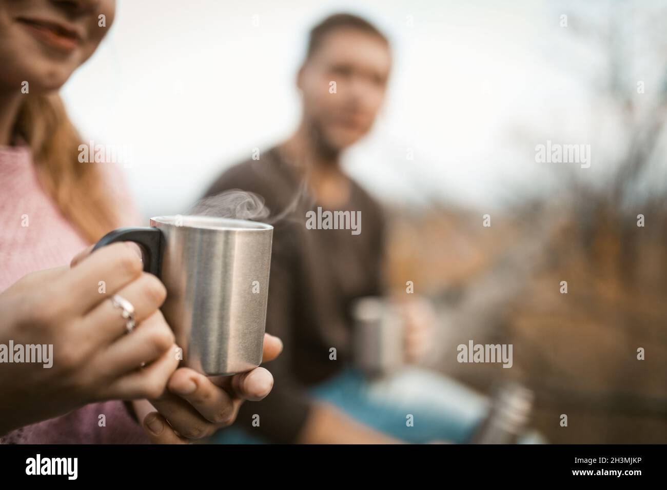 Deux touristes boivent une boisson chaude dans la nature.Accent sélectif sur la tasse de camping en métal avec la vapeur d'un café chaud ou thé dans le han femelle Banque D'Images