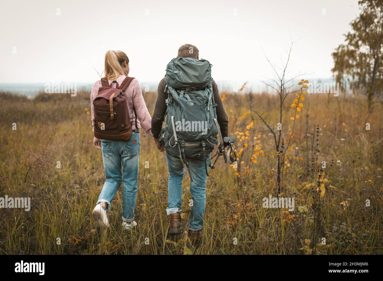 Randonnée dans la nature automnale, couple de routards fait leur chemin à travers le champ, vue arrière de l'homme et la femme avec des sacs à dos et h Banque D'Images