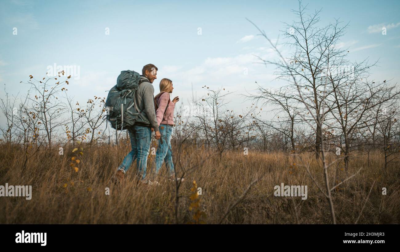 Deux voyageurs marchant dans un champ d'automne tenant les mains.Touristes à pleine hauteur sur un fond de ciel bleu et Banque D'Images