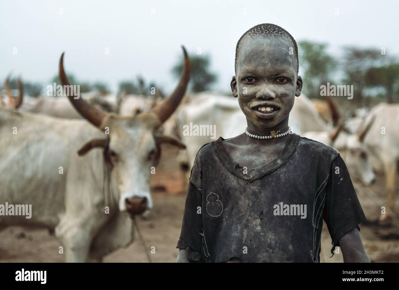 TRIBU MUNDARI, SOUDAN DU SUD - 11 MARS 2020 : un jeune berger dans des chiffons souriant à la caméra avec intérêt tout en se tenant contre le troupeau de Banque D'Images