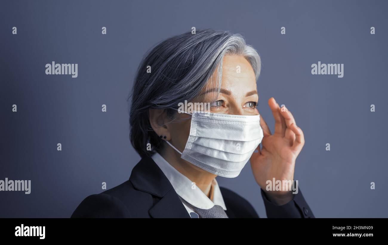 Femme d'affaires mature masque correct sur son visage.Concentrez-vous sur les yeux des femmes.Portrait d'une femme aux cheveux gris sur fond bleu gris.CLO Banque D'Images