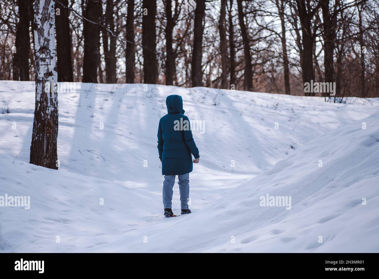 Marchez le long de la journée hivernale glacielle.La jeune femme caucasienne vêtue de vêtements chauds se trouve sur une route enneigée dans la forêt parmi les grands arbres et bénéficie de l'éblouissement du soleil sur la neige Banque D'Images