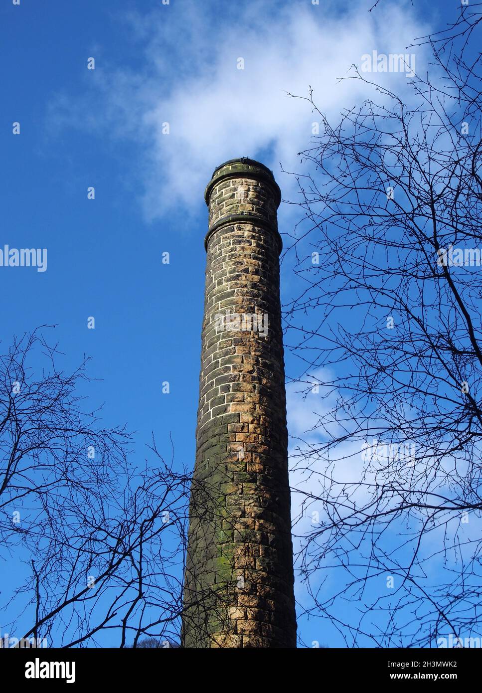 Vue verticale d'une vieille cheminée en pierre dans un moulin en ruines entouré d'arbres contre un ciel bleu nuageux dans la vallée de Colden ouest y Banque D'Images