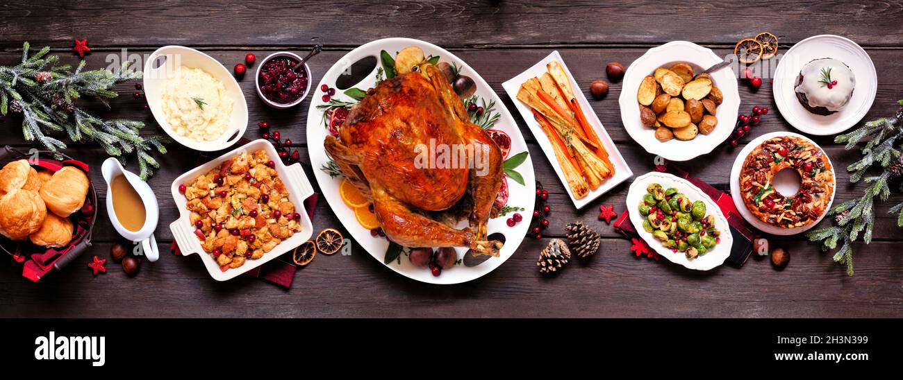 Dîner traditionnel dinde de Noël.Vue de dessus scène de table panoramique sur fond de bannière en bois sombre.Dinde, pommes de terre et accompagnements, vinaigrette, gâteau aux fruits Banque D'Images