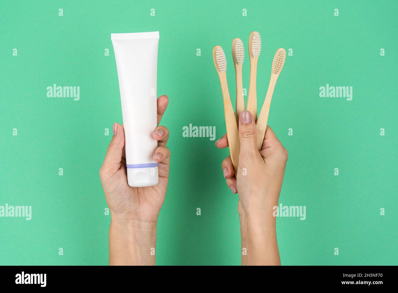 Brosses à dents en bambou et un tube de dentifrice dans les mains des femmes sur fond de menthe.Tendances actuelles de la consommation consciente. Banque D'Images